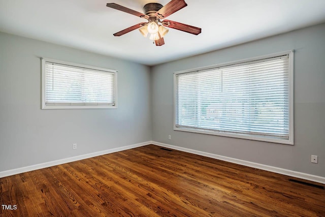 empty room with dark wood-style flooring, a ceiling fan, baseboards, and a healthy amount of sunlight