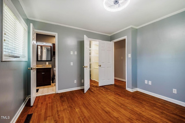 unfurnished bedroom featuring connected bathroom, baseboards, wood finished floors, visible vents, and ornamental molding
