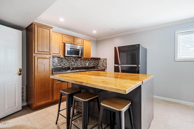 kitchen with light tile patterned flooring, freestanding refrigerator, stainless steel microwave, tasteful backsplash, and butcher block counters