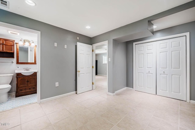 unfurnished bedroom with visible vents, light tile patterned flooring, baseboards, connected bathroom, and a sink
