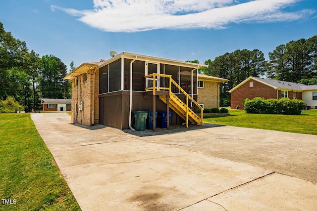 back of house with a lawn, a sunroom, stairway, brick siding, and concrete driveway