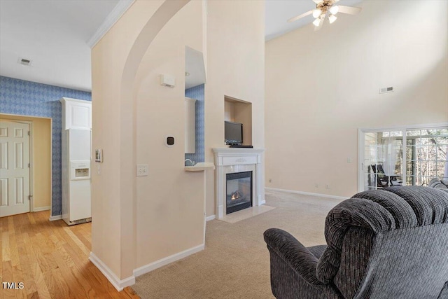 living area featuring ceiling fan, a high ceiling, baseboards, a tile fireplace, and visible vents