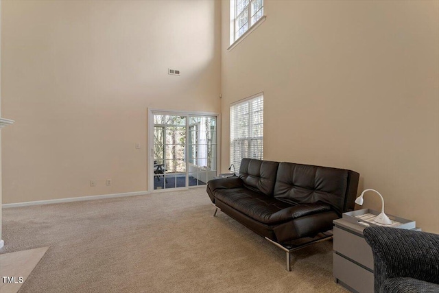 living area featuring baseboards, visible vents, light carpet, and a towering ceiling