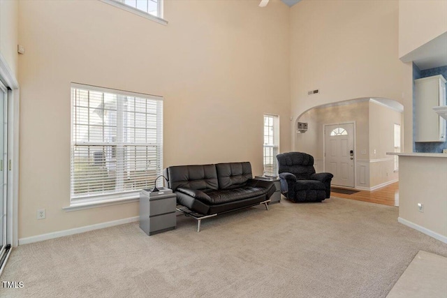 living area with baseboards, light colored carpet, visible vents, and a towering ceiling