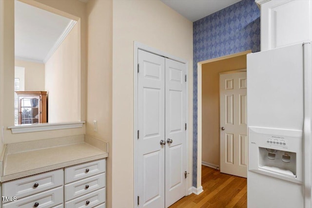 hallway with light wood-style floors, ornamental molding, baseboards, and wallpapered walls