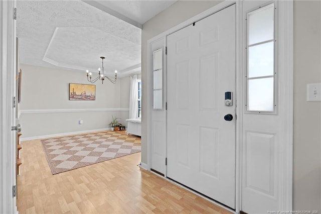 entryway featuring baseboards, a raised ceiling, a textured ceiling, a chandelier, and light wood-style flooring