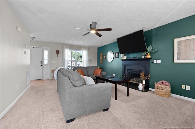carpeted living area with visible vents, baseboards, ceiling fan, a textured ceiling, and a fireplace with flush hearth