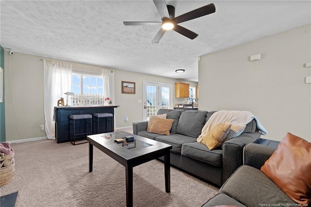 living area with baseboards, a textured ceiling, ceiling fan, and light carpet