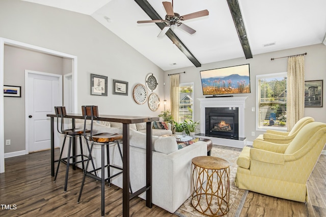 living area featuring visible vents, a glass covered fireplace, wood finished floors, a healthy amount of sunlight, and vaulted ceiling with beams