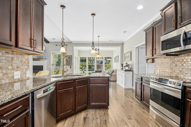 kitchen featuring tasteful backsplash, a sink, stainless steel appliances, a peninsula, and light wood-type flooring