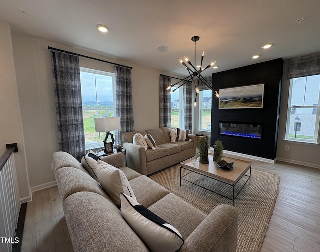 living area featuring baseboards, a wealth of natural light, a notable chandelier, and light wood-type flooring