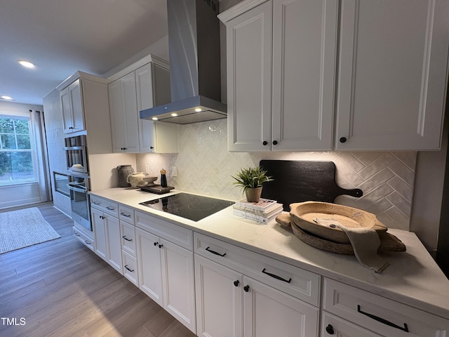 5906 Dunzo Dr, Raleigh, NC 27617 - kitchen with wall chimney range hood, black electric stovetop, light wood-style floors, light countertops, and recessed lighting