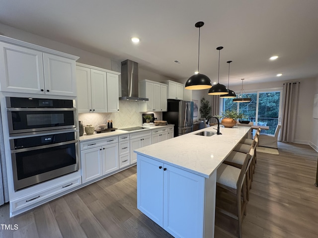 5906 Dunzo Dr, Raleigh, NC 27617 - kitchen with stainless steel appliances, wall chimney exhaust hood, a kitchen island with sink, dark wood finished floors, and tasteful backsplash
