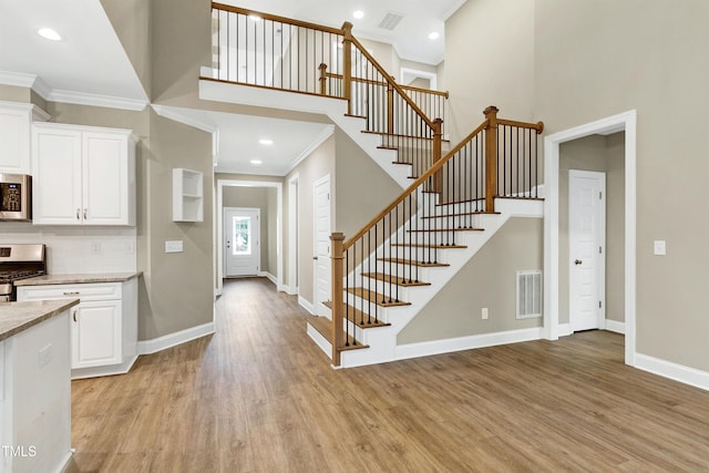 interior space with visible vents, ornamental molding, light wood-style floors, and a towering ceiling