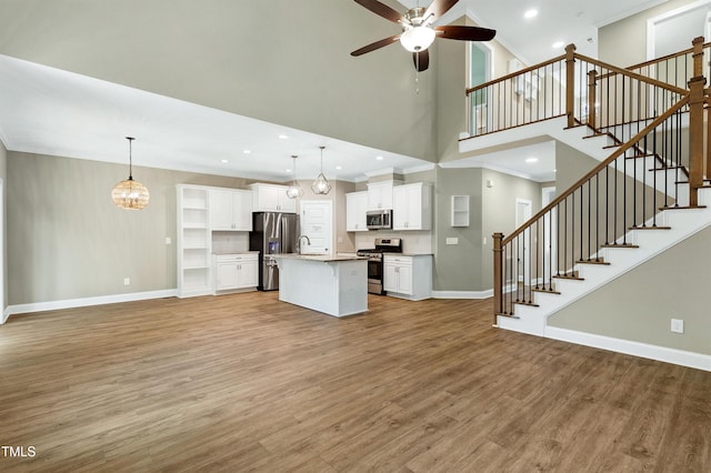 unfurnished living room with a towering ceiling, baseboards, ceiling fan with notable chandelier, light wood-style floors, and ornamental molding