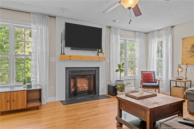 living area with light wood-style floors, a fireplace, a ceiling fan, and a textured ceiling