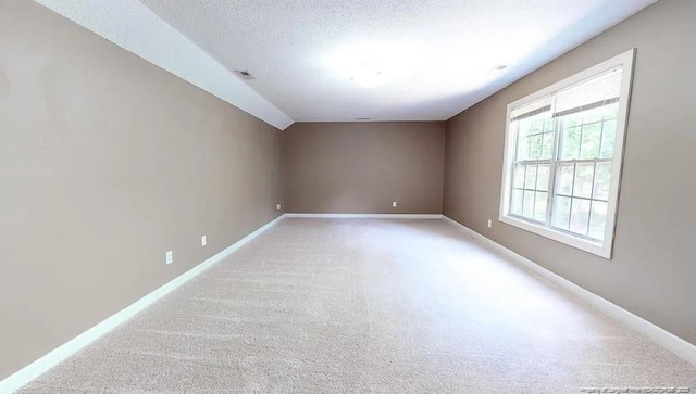 unfurnished room featuring visible vents, baseboards, light colored carpet, a textured ceiling, and vaulted ceiling