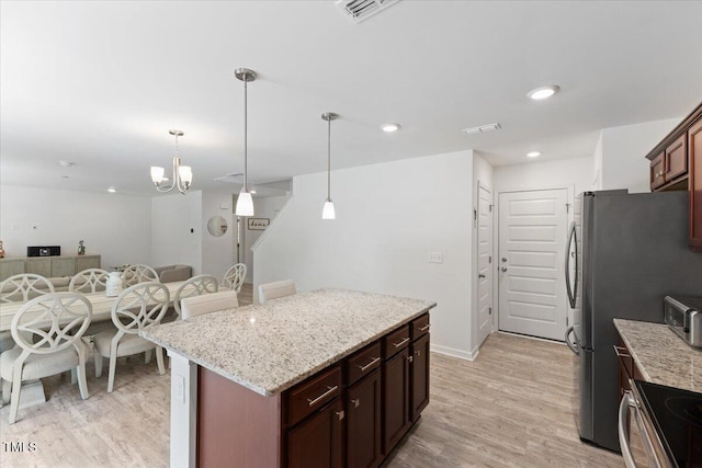 kitchen featuring pendant lighting, a center island, light stone countertops, open floor plan, and light wood-style flooring