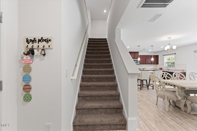 stairs with a chandelier, recessed lighting, wood finished floors, and visible vents