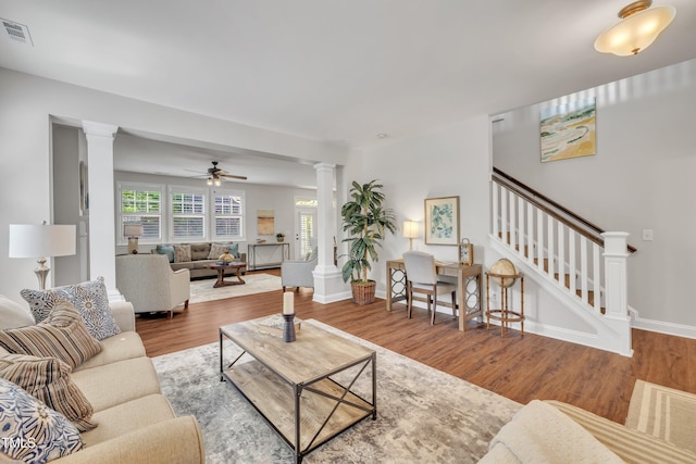 living room featuring ceiling fan, wood finished floors, ornate columns, visible vents, and stairway
