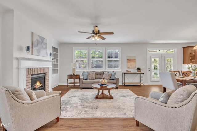 living area featuring a brick fireplace, ceiling fan, wood finished floors, and built in features
