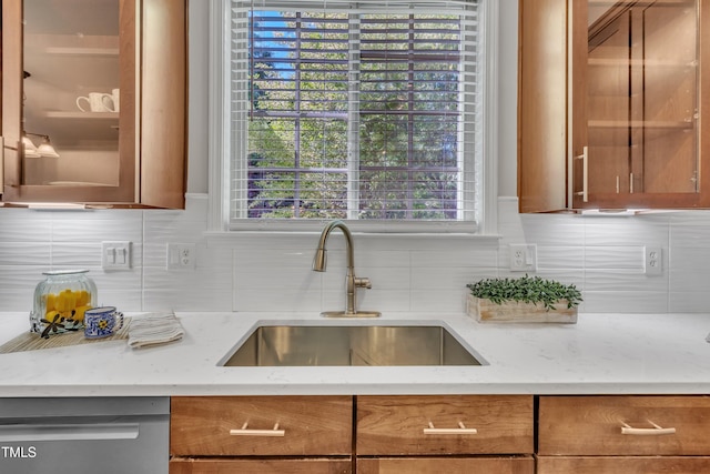 kitchen with a sink, decorative backsplash, stainless steel dishwasher, and brown cabinets