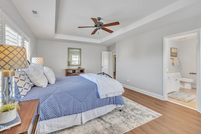 bedroom with visible vents, wood finished floors, a tray ceiling, and multiple windows