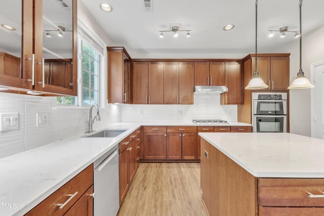 kitchen with brown cabinets, a sink, stainless steel appliances, under cabinet range hood, and visible vents