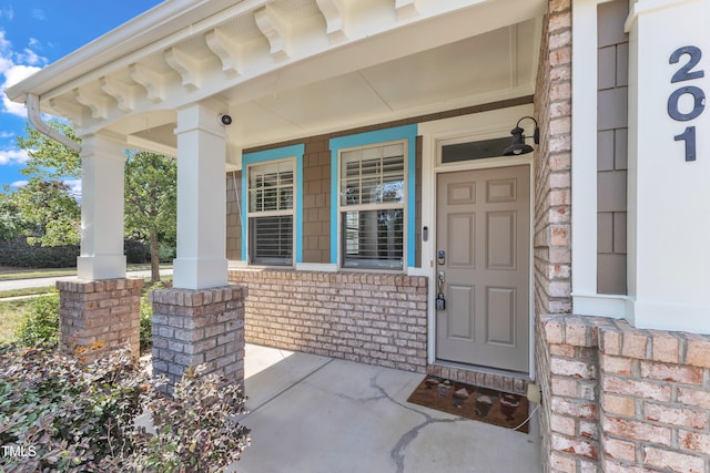 entrance to property featuring a porch and brick siding