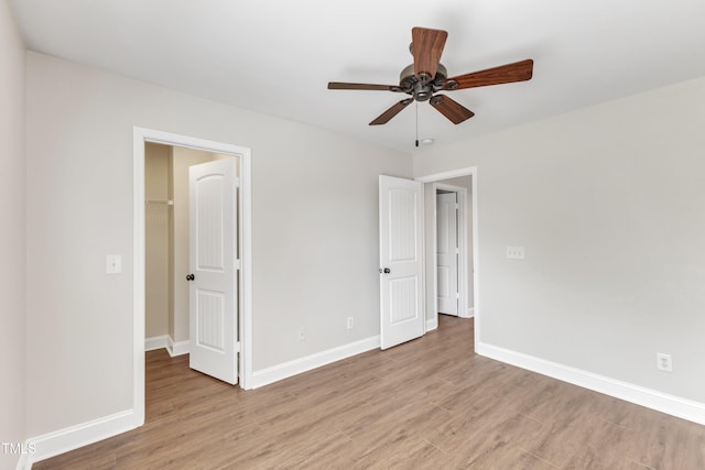 unfurnished bedroom featuring light wood-type flooring, a ceiling fan, baseboards, and a spacious closet