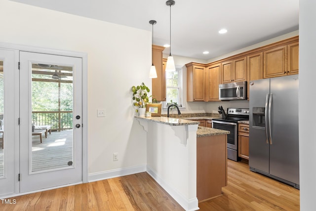 kitchen with stainless steel appliances, light stone counters, light wood-type flooring, and a peninsula