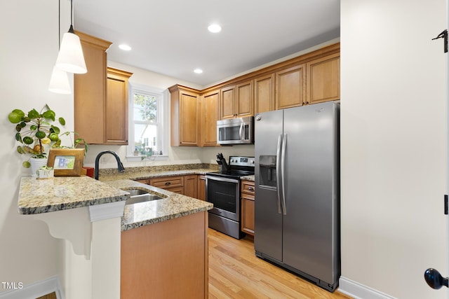 kitchen featuring a breakfast bar area, a sink, light stone counters, a peninsula, and stainless steel appliances