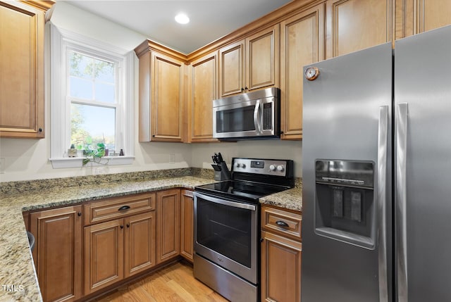 kitchen with brown cabinets, stainless steel appliances, light stone counters, and light wood-style floors