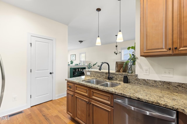 kitchen with light stone countertops, light wood-type flooring, brown cabinets, dishwasher, and a sink