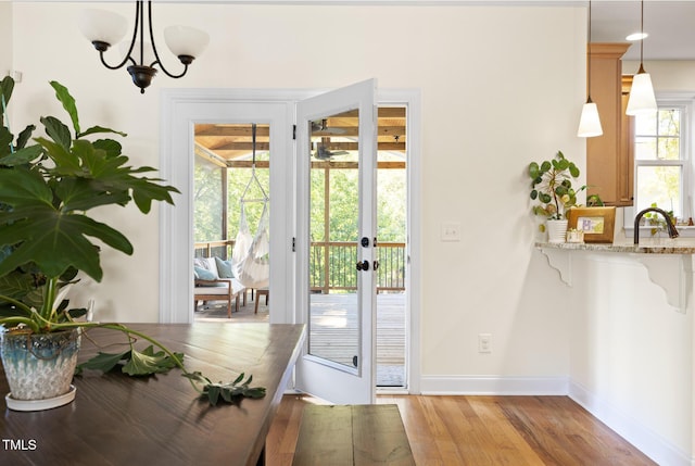 doorway to outside featuring baseboards, light wood finished floors, and an inviting chandelier