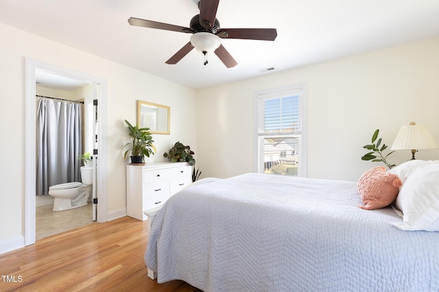 bedroom featuring ceiling fan, visible vents, baseboards, light wood-style floors, and ensuite bathroom