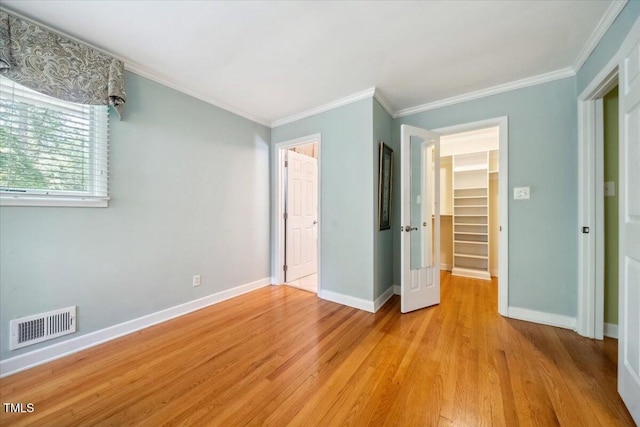unfurnished bedroom featuring a walk in closet, baseboards, light wood-style flooring, and visible vents