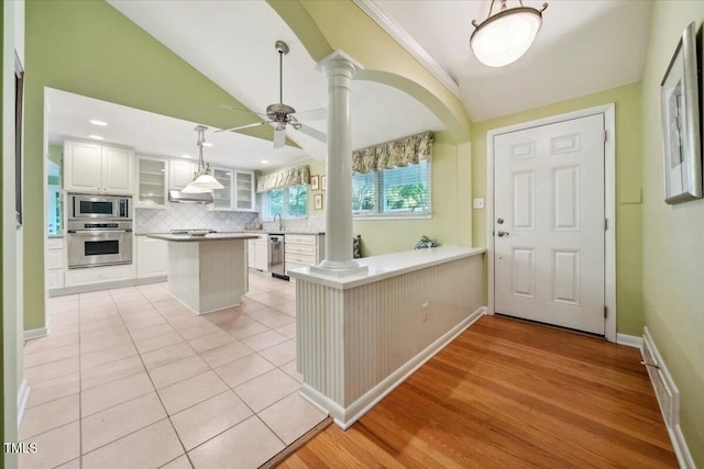 interior space featuring decorative columns, appliances with stainless steel finishes, tasteful backsplash, vaulted ceiling, and glass insert cabinets
