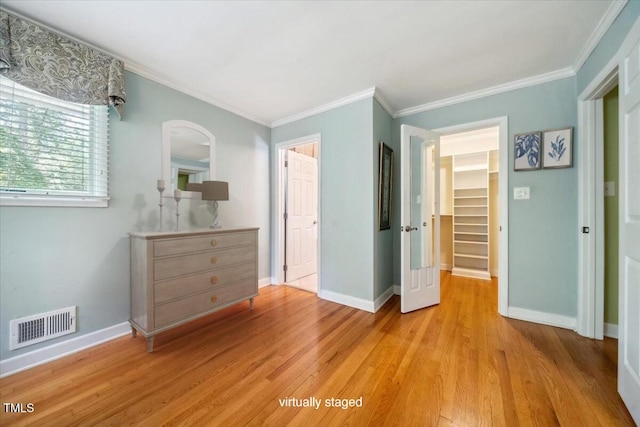 unfurnished bedroom with a walk in closet, baseboards, light wood-type flooring, visible vents, and ornamental molding