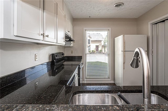 kitchen featuring electric range, a textured ceiling, white cabinets, freestanding refrigerator, and under cabinet range hood