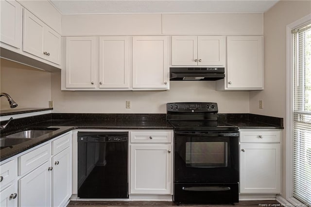 kitchen with dark stone counters, under cabinet range hood, white cabinets, a sink, and black appliances