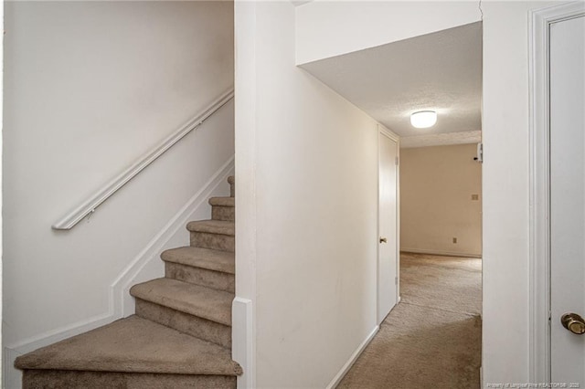 stairway featuring baseboards, carpet flooring, and a textured ceiling