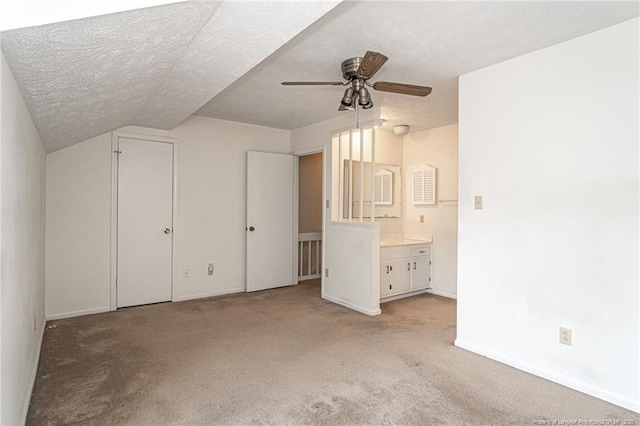 unfurnished bedroom with light carpet, baseboards, a textured ceiling, ensuite bath, and vaulted ceiling