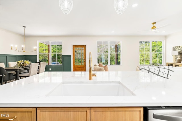 kitchen with light stone counters, a sink, dishwasher, a chandelier, and open floor plan