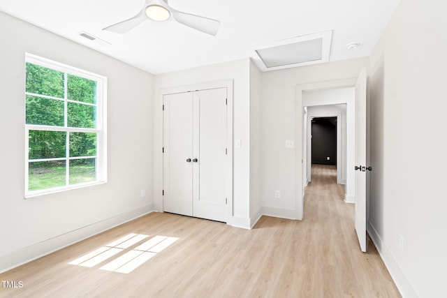 unfurnished bedroom featuring a closet, light wood-style floors, attic access, baseboards, and ceiling fan