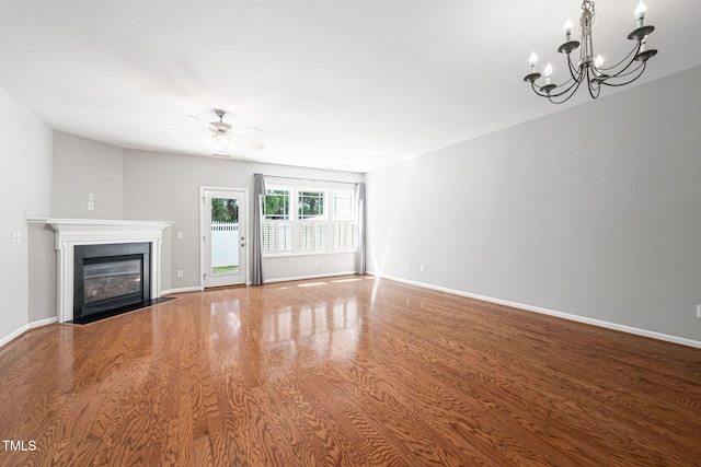 unfurnished living room featuring baseboards, a fireplace with flush hearth, wood finished floors, and ceiling fan with notable chandelier