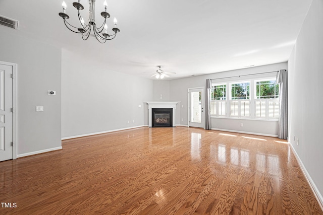 unfurnished living room featuring light wood finished floors, a glass covered fireplace, ceiling fan with notable chandelier, baseboards, and visible vents