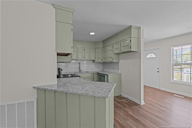 kitchen featuring visible vents, a peninsula, wood finished floors, backsplash, and green cabinets