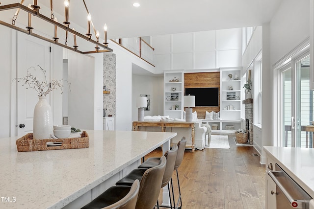 kitchen featuring a high ceiling, light stone countertops, a breakfast bar area, wood finished floors, and stainless steel dishwasher