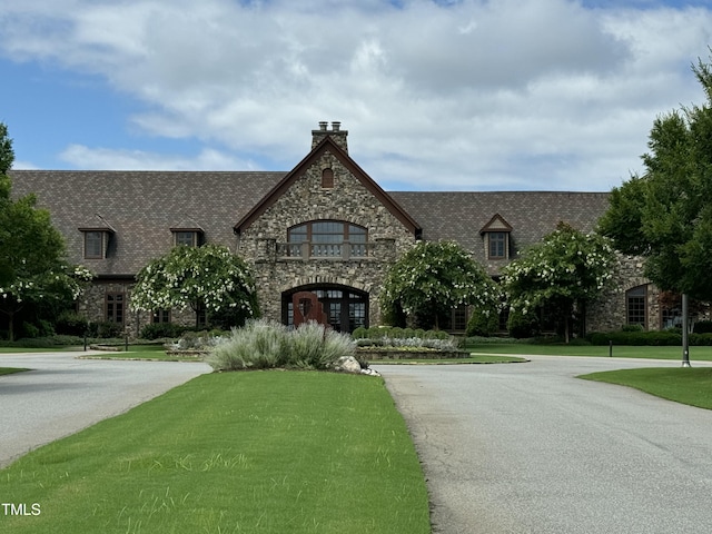 view of front of house with a front yard, a chimney, and stone siding